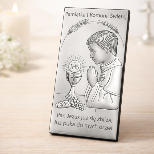 Srebrny obrazek komunijny dla chłopca na jasnej komodzie – ujęcie pod kątem 30–45 stopni