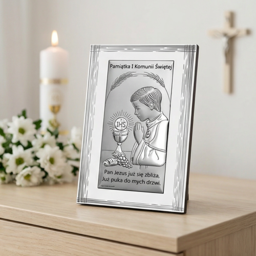 Pamiątka na I Komunię Świętą – obrazek srebrny komunijny dla chłopca w aranżacji na komodzie, dekoracja ze świecą i kwiatami