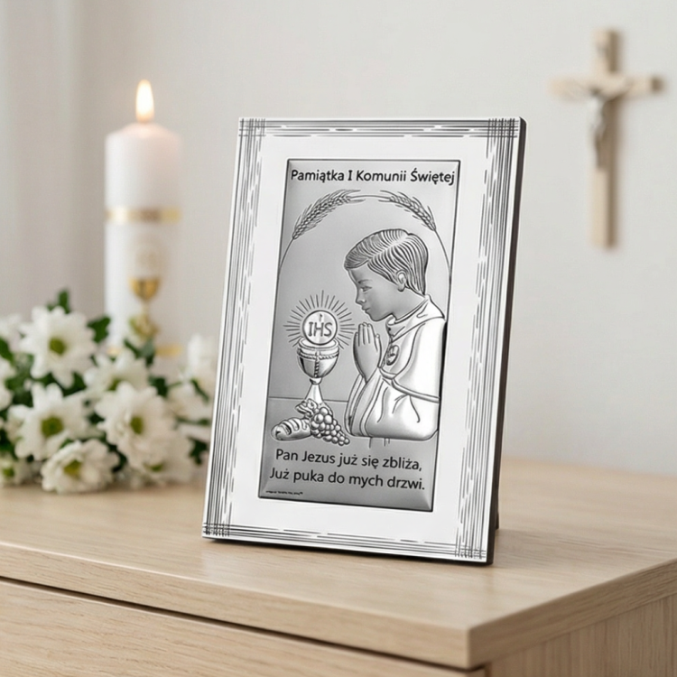 Pamiątka na I Komunię Świętą – obrazek srebrny komunijny dla chłopca w aranżacji na komodzie, dekoracja ze świecą i kwiatami