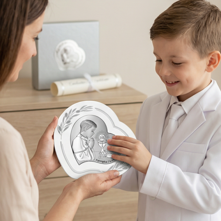 Prezent na I Komunię dla chłopca – dziecko w stroju komunijnym ogląda srebrny obrazek serce z motywem IHS, ujęcie lifestyle