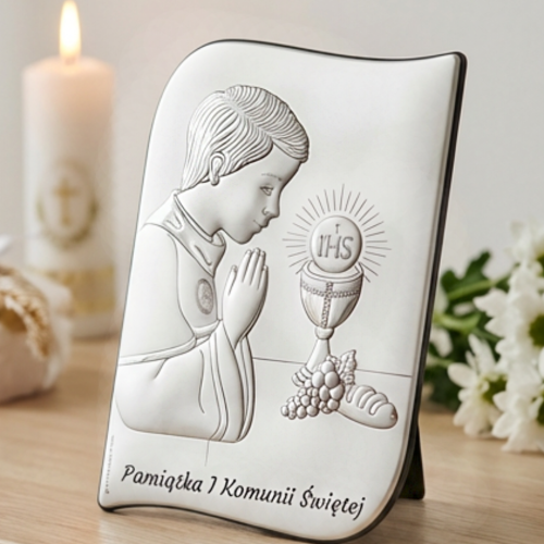 Pamiątka I Komunii Świętej – srebrny obrazek falowany dla chłopca z motywem IHS i kielicha, aranżacja na komodzie ze świecą