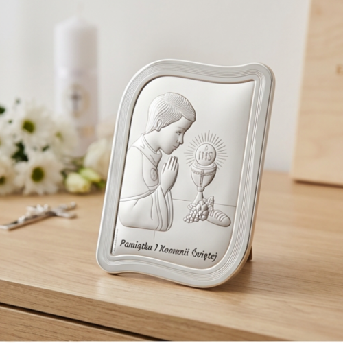 Pamiątka I Komunii Świętej – srebrny obrazek komunijny dla chłopca w falowanej ramce, ujęcie pod kątem na komodzie