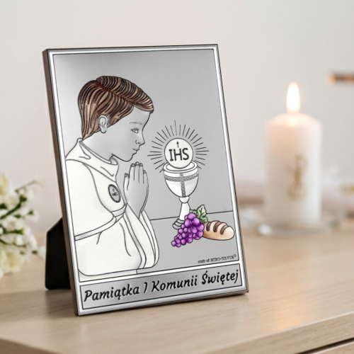 Pamiątka I Komunii Świętej – srebrny prostokątny obrazek komunijny dla chłopca z hostią IHS, aranżacja na komodzie, świeca i krzyż w tle