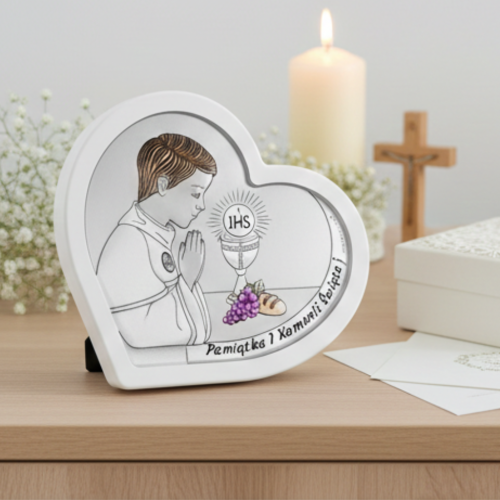 Pamiątka I Komunii Świętej – srebrny obrazek serce dla chłopca z motywem IHS, aranżacja na komodzie ze świecą, krzyżem i opakowaniem