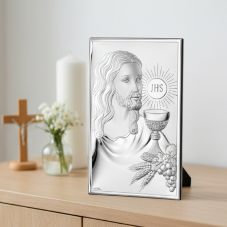 Obrazek komunijny z Jezusem i kielichem JHS ustawiony na komodzie obok krzyża i świecy