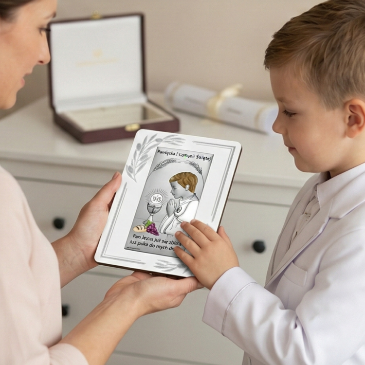 Chłopiec w albie ogląda pamiątkę Pierwszej Komunii – srebrny obrazek z hostią IHS i napisem Pamiątka I Komunii Świętej