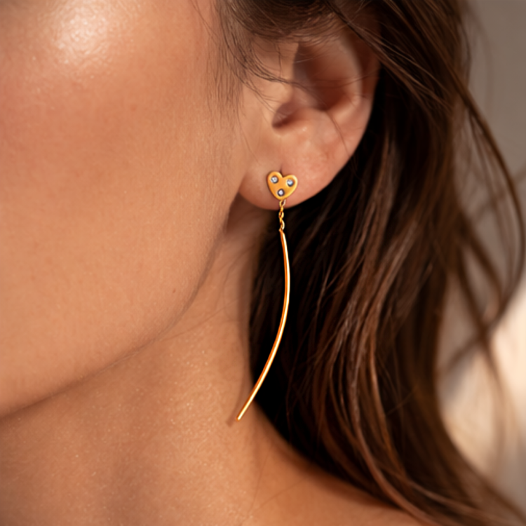Złoty kolczyk wiszący z motywem serca i trzema cyrkoniami na uchu