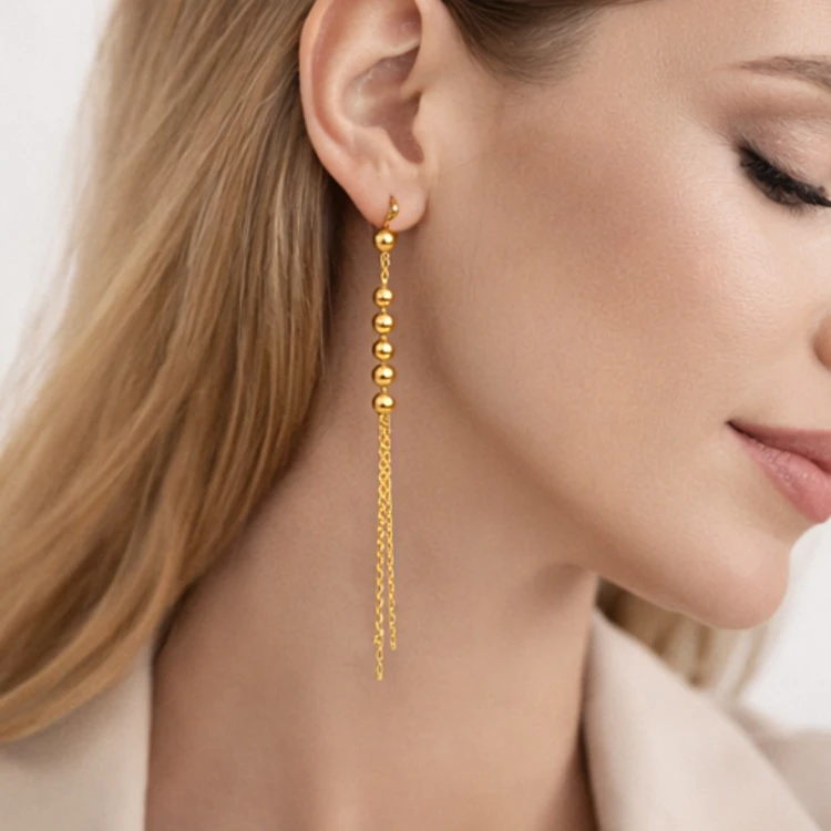 Złoty kolczyk wiszący z kuleczkami i podwójnym łańcuszkiem na uchu modelki