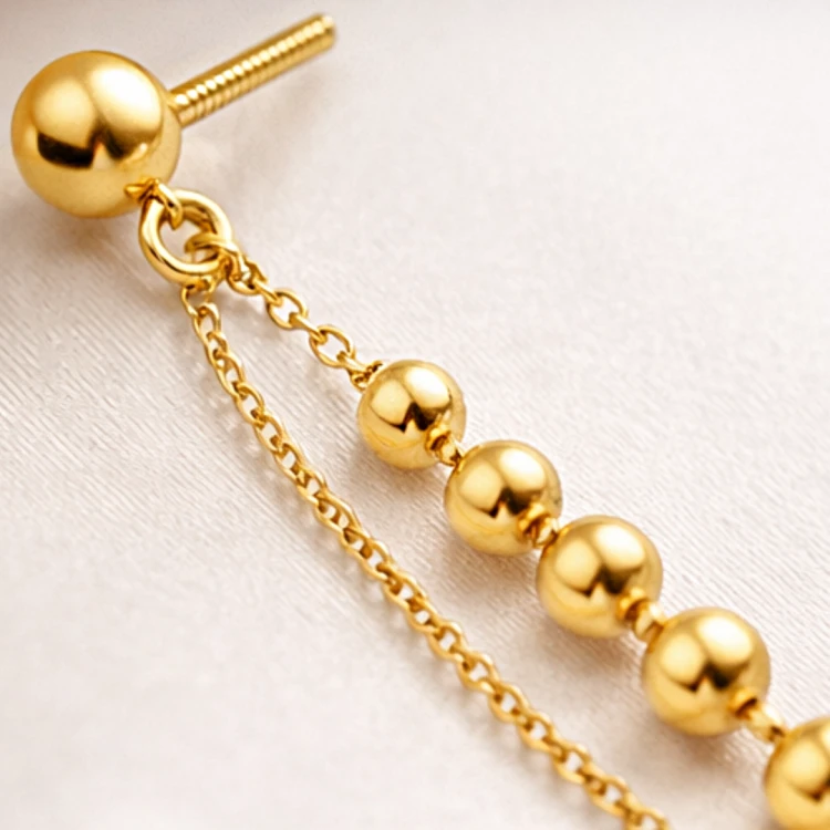 Zbliżenie złotego kolczyka wiszącego z kuleczkami i delikatnym łańcuszkiem
