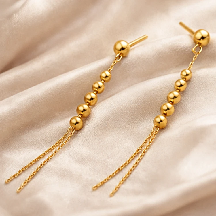 Złote kolczyki wiszące z kuleczkami i podwójnym łańcuszkiem na satynowej tkaninie