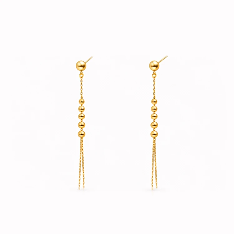 Złote kolczyki wiszące z kuleczkami i podwójnym łańcuszkiem na jasnym tle