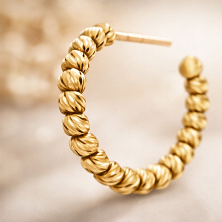 Zbliżenie złotego kolczyka koła z ryflowanymi kuleczkami