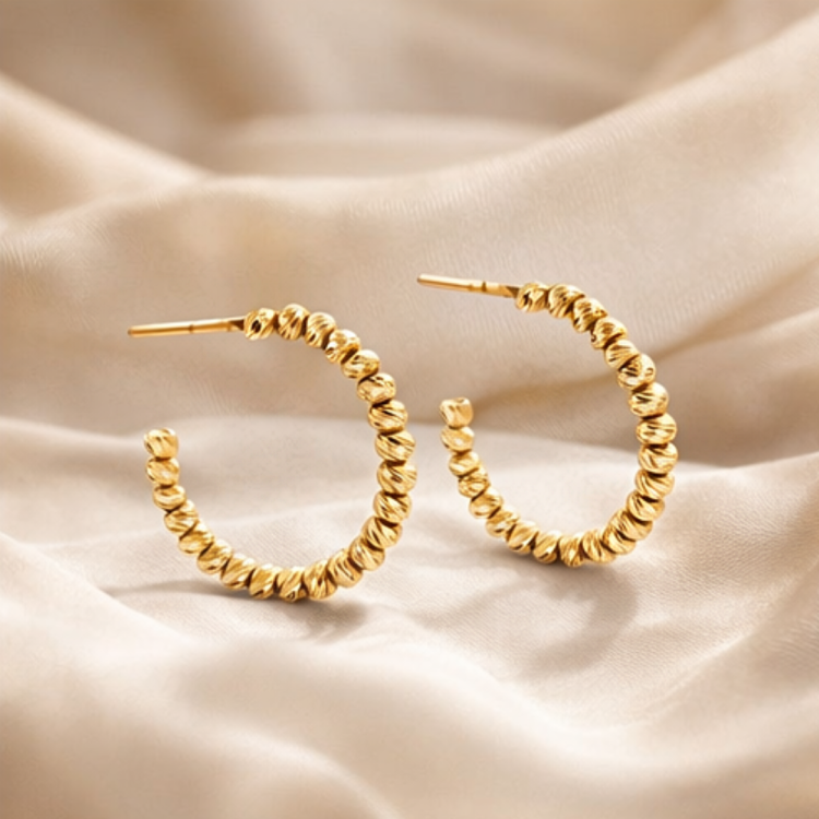 Złote kolczyki koła z ryflowanymi kuleczkami na satynowej tkaninie