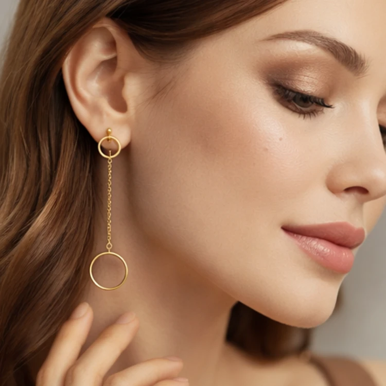 Złoty kolczyk wiszący z łańcuszkiem i okrągłą zawieszką prezentowany na uchu modelki