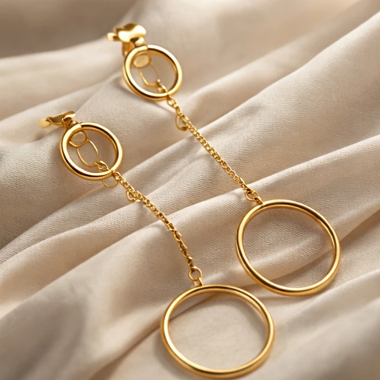 Para złotych kolczyków wiszących z okrągłymi zawieszkami ułożona na jasnej eleganckiej tkaninie