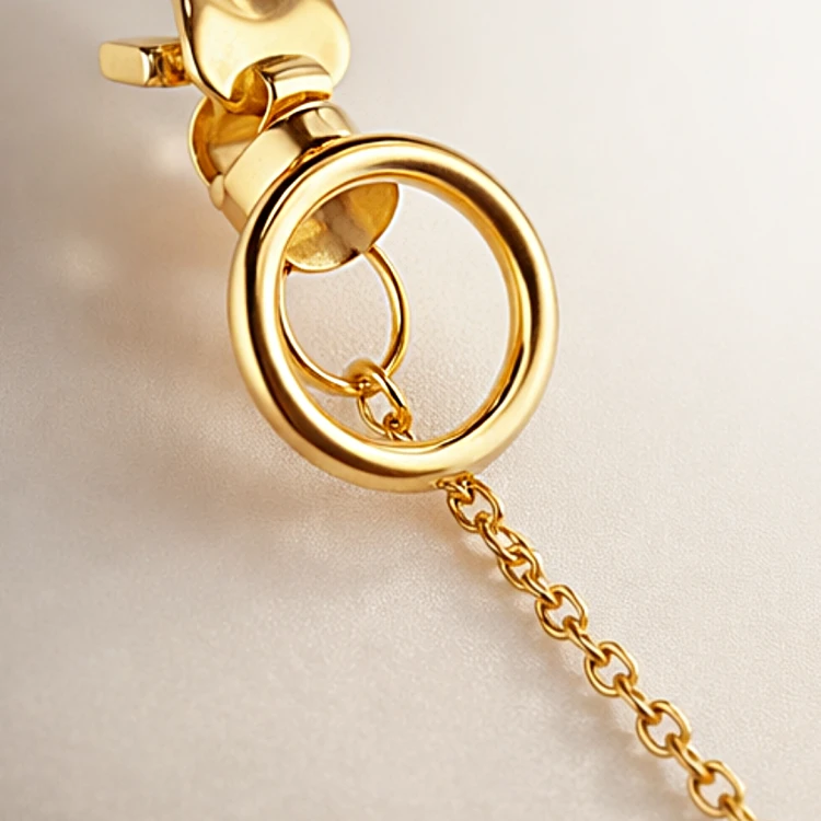 Zbliżenie na złoty kolczyk wiszący z okrągłym elementem i delikatnym łańcuszkiem