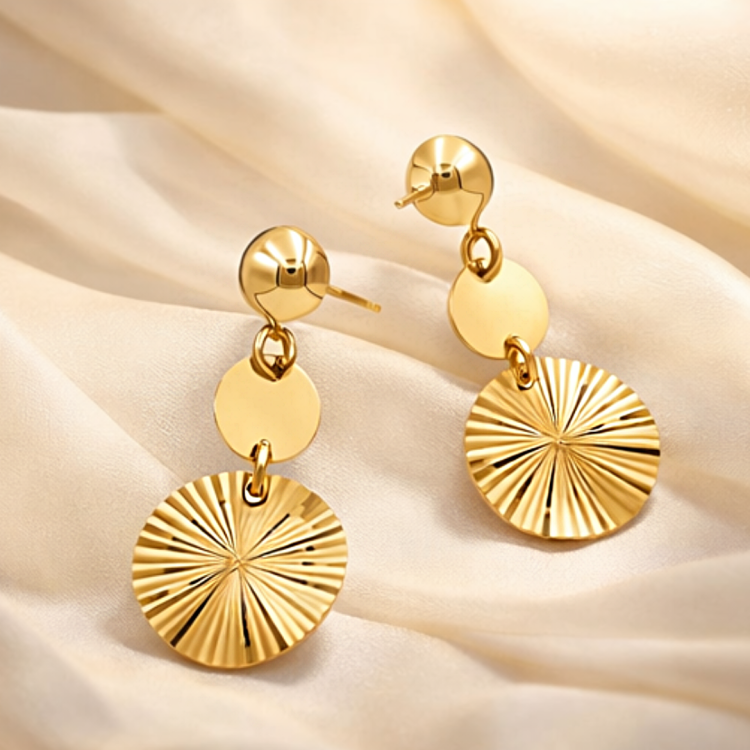 Złote kolczyki wiszące z okrągłymi zawieszkami ułożone na jasnej tkaninie