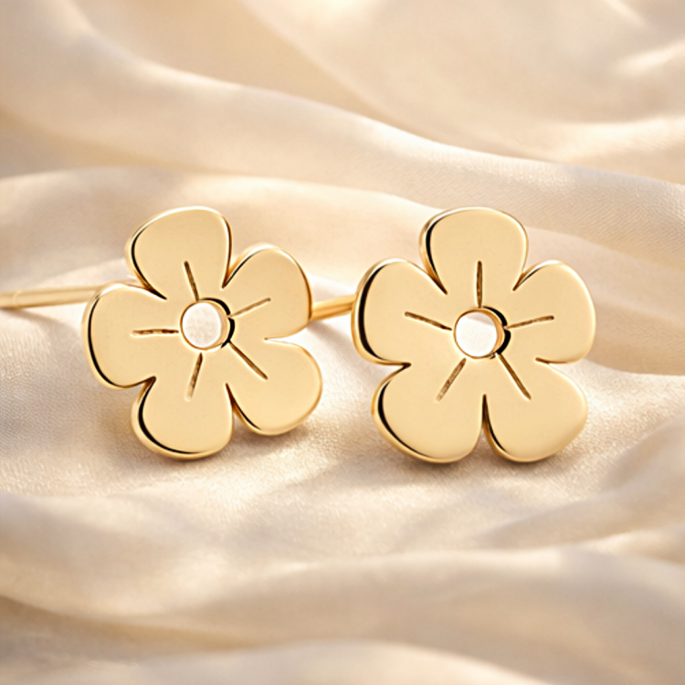 Złote kolczyki sztyfty kwiatki ułożone na jasnej tkaninie