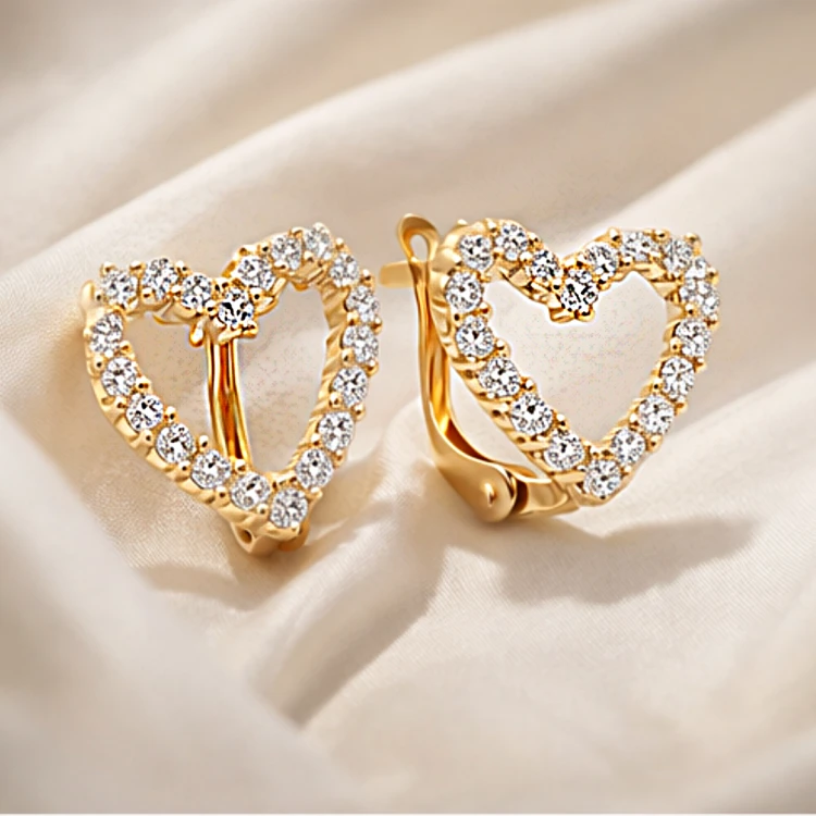 Złote kolczyki serca z cyrkoniami ułożone na jasnej tkaninie