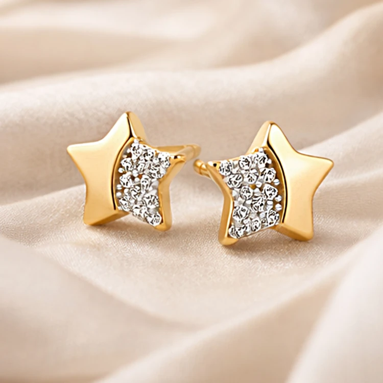 Złote kolczyki sztyfty gwiazdki z cyrkoniami ułożone na jasnej tkaninie