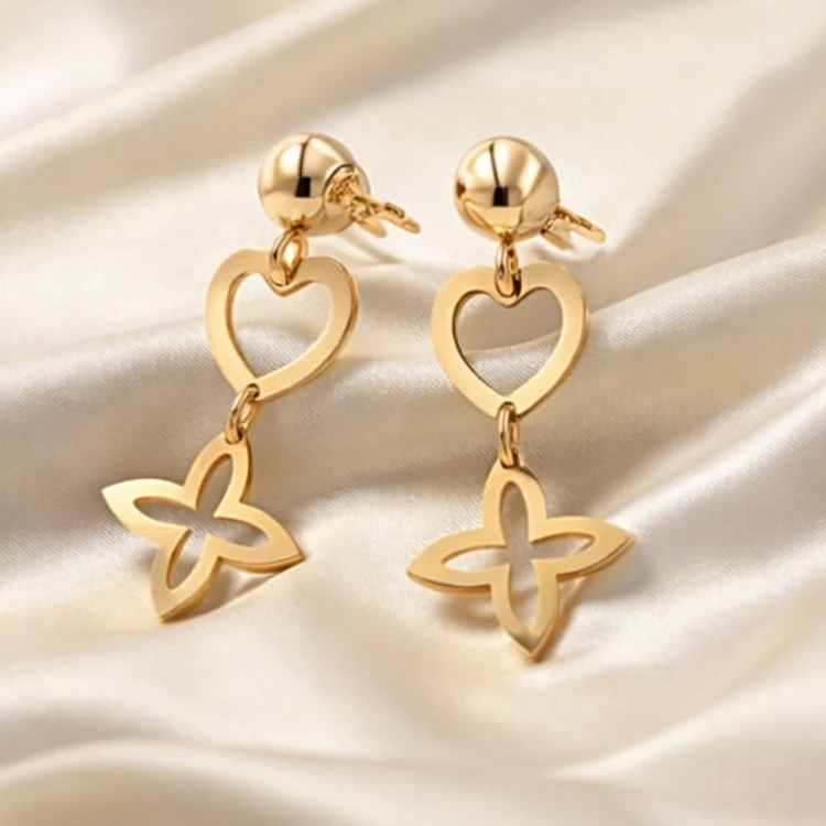 Złote kolczyki wiszące z ażurowym sercem i koniczyną na jasnej tkaninie