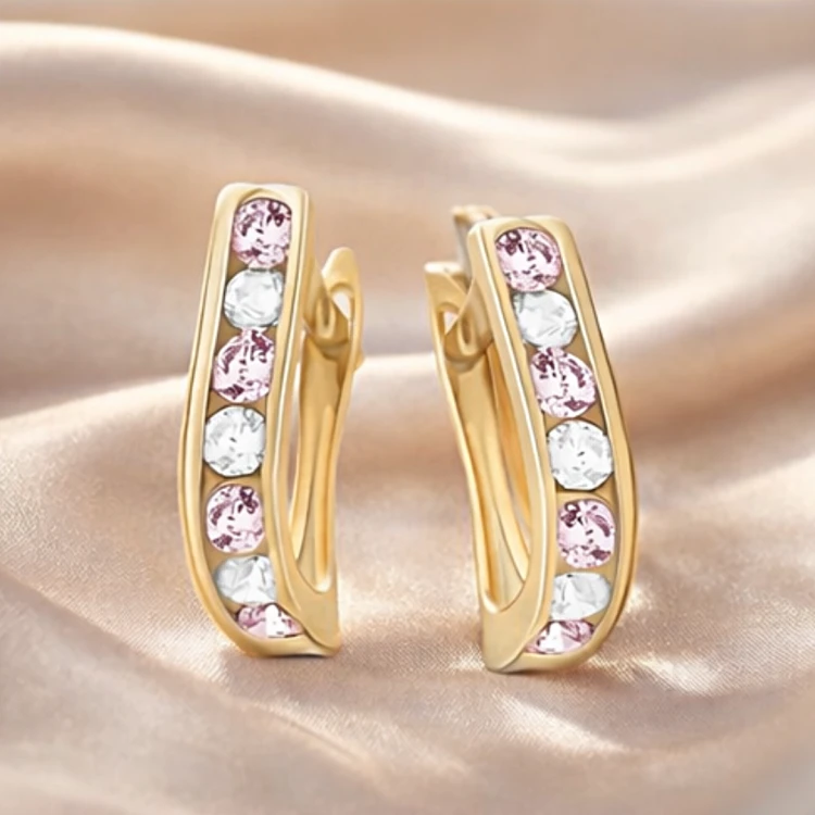 Złote kolczyki zatrzaskowe z różowymi i białymi cyrkoniami na jasnej tkaninie