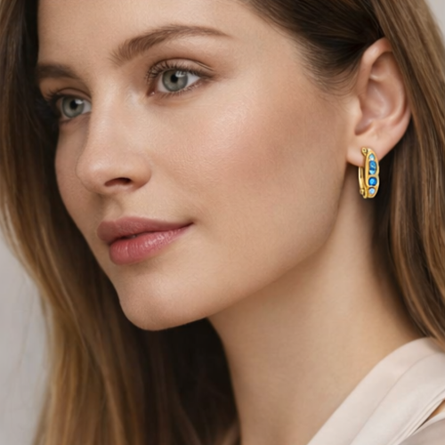 Modelka w złotych kolczykach zatrzaskowych z niebieskimi i białymi cyrkoniami