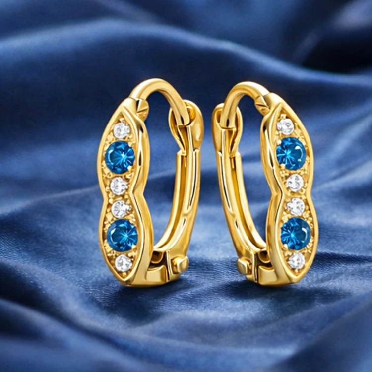 Złote kolczyki zatrzaskowe z niebieskimi i białymi cyrkoniami na granatowej tkaninie