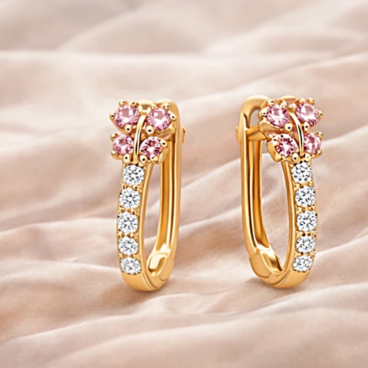 Złote kolczyki koła z różowymi i białymi cyrkoniami na jasnej satynowej tkaninie