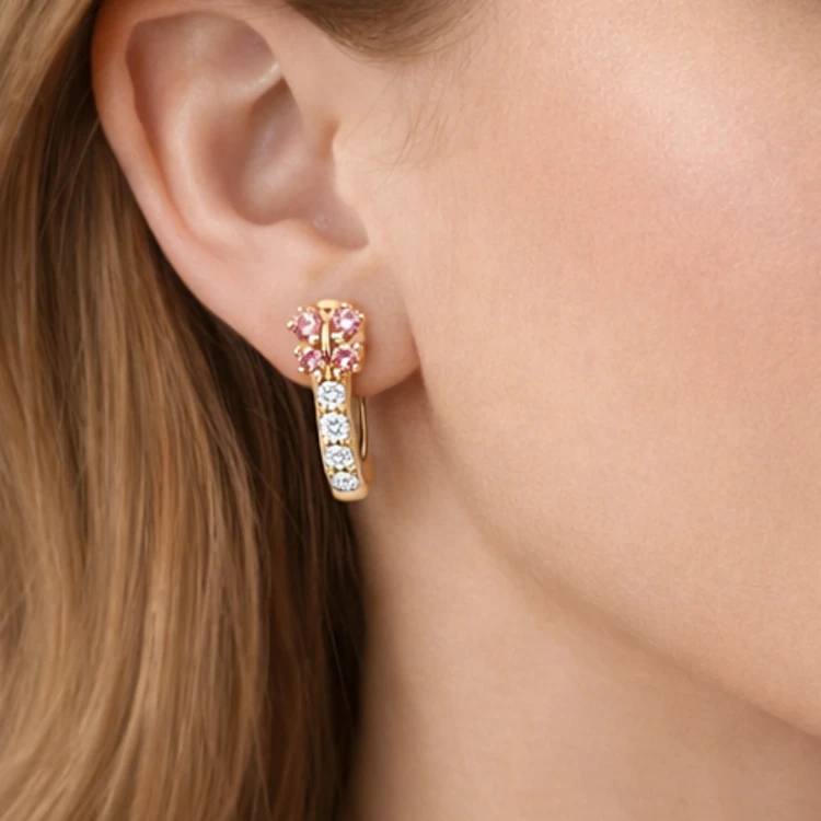 Złoty kolczyk koło z różowymi i białymi cyrkoniami na uchu kobiety