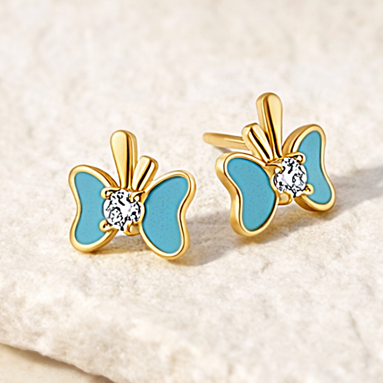 Złote kolczyki w kształcie motyla z niebieskimi skrzydłami na jasnym tle