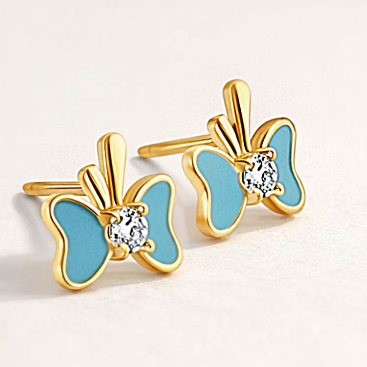 Złote kolczyki motylki z niebieskim wykończeniem i jasnym kamieniem w zbliżeniu
