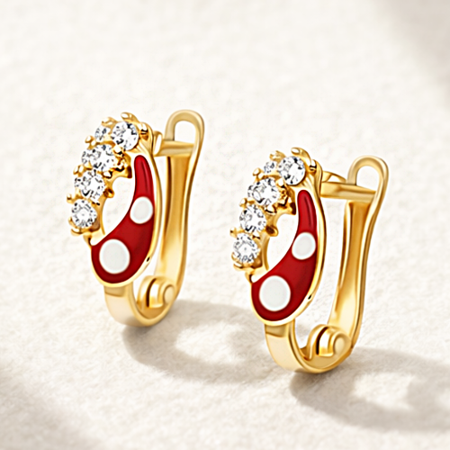 Złote kolczyki z czerwoną emalią, białymi detalami i połyskującymi kamieniami na jasnym tle