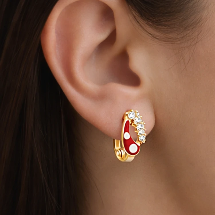 Złoty kolczyk z czerwonym motywem łezki i białymi kamieniami prezentowany na uchu