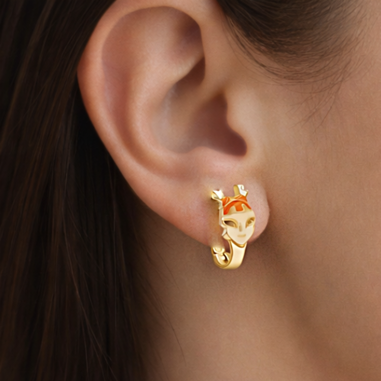 Złoty kolczyk z motywem stylizowanej twarzy prezentowany na uchu