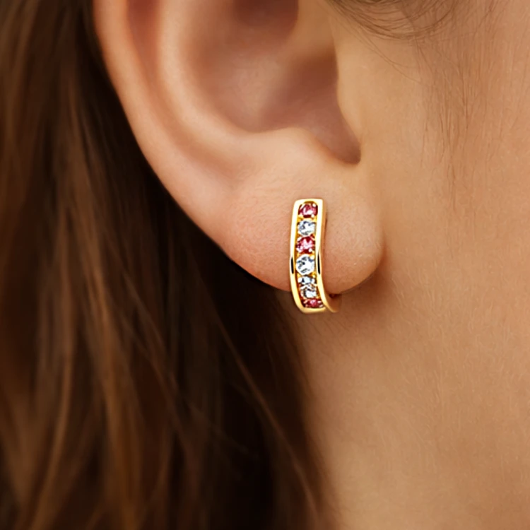 Złoty kolczyk koło z różowymi i białymi kamieniami na uchu