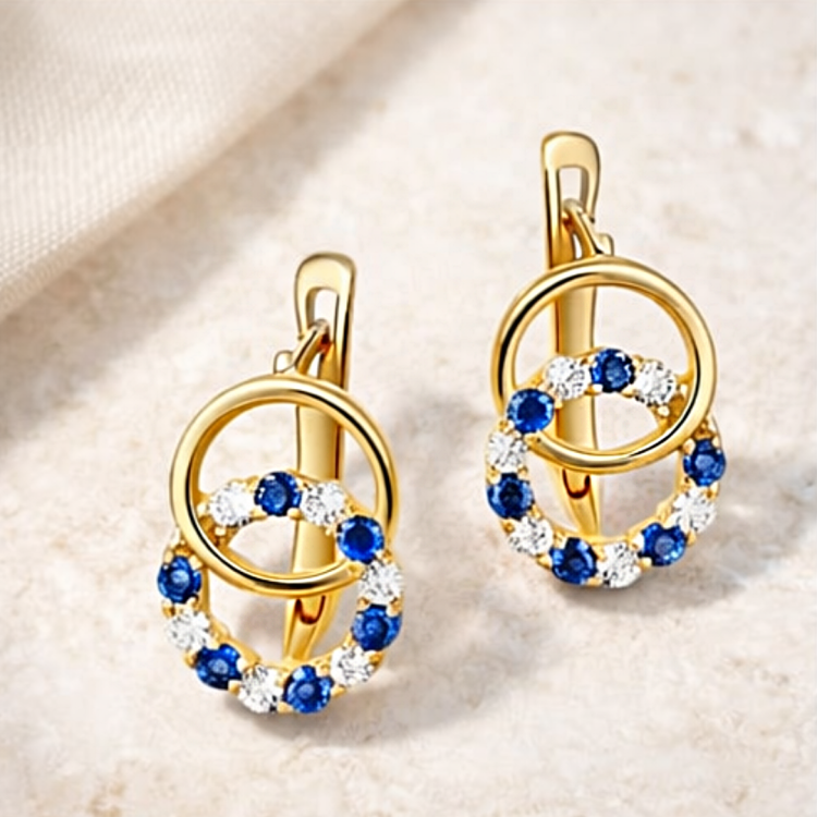 Para złotych kolczyków z okrągłymi zawieszkami i niebieskimi, białymi kamieniami – ujęcie pod kątem