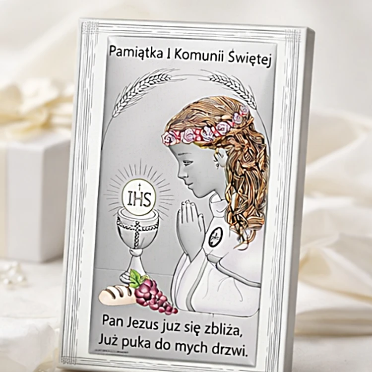 Obrazek komunijny dla dziewczynki w srebrnej ramce ustawiony na jasnym tle prezentowym