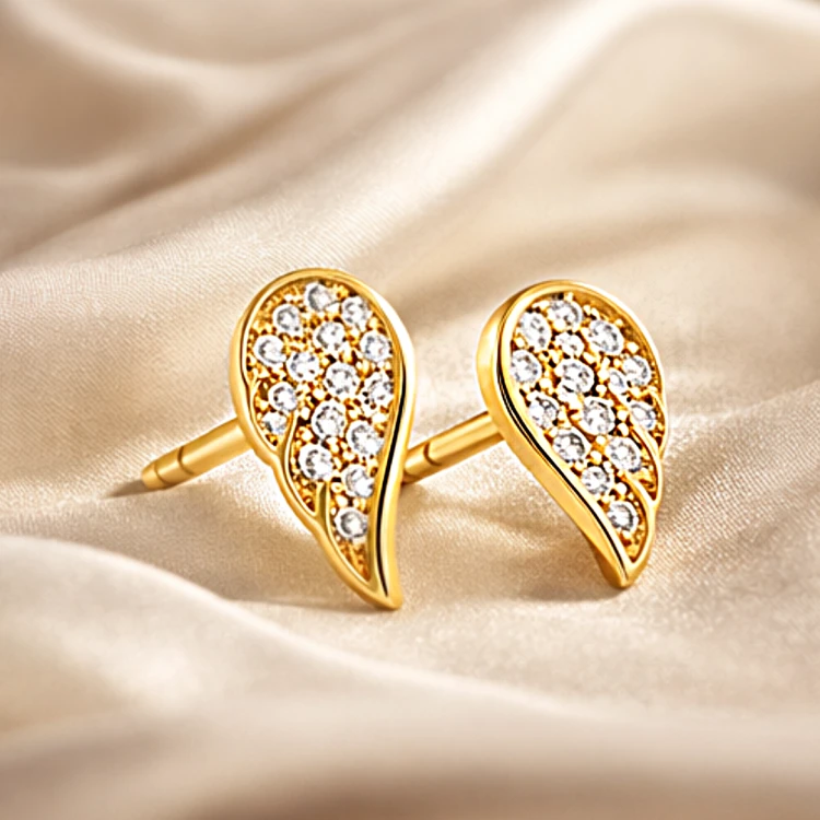 Złote kolczyki sztyfty w kształcie skrzydła z cyrkoniami na satynowym tle