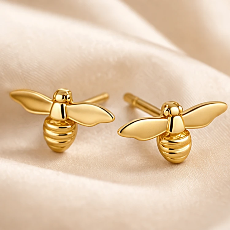 Para złotych kolczyków pszczół na jasnej satynowej tkaninie