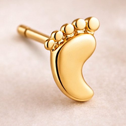 Zbliżenie złotego kolczyka w kształcie stópki z gładkim połyskiem