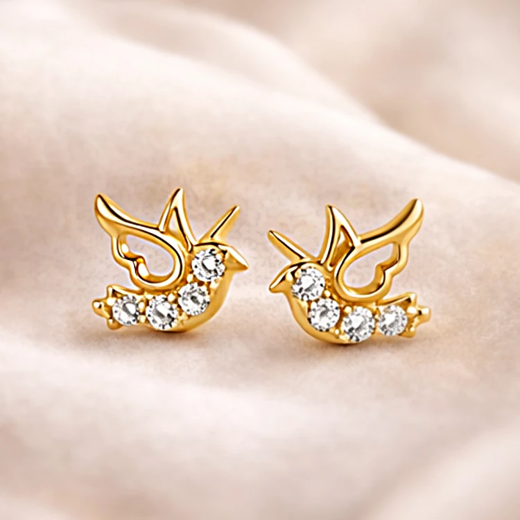 Para złotych kolczyków jaskółek z cyrkoniami na jasnej tkaninie