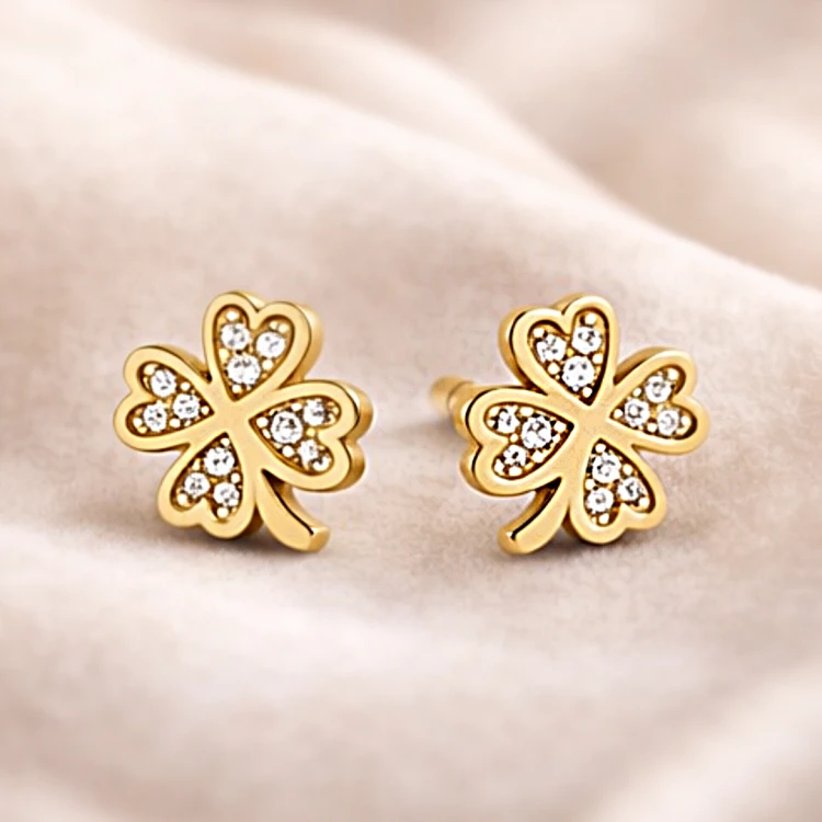 Para złotych kolczyków w kształcie koniczyny z cyrkoniami na jasnej tkaninie