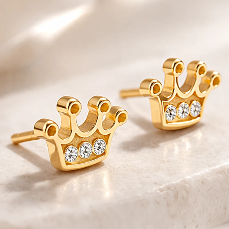 Złote kolczyki korony z cyrkoniami na jasnym kamiennym podłożu