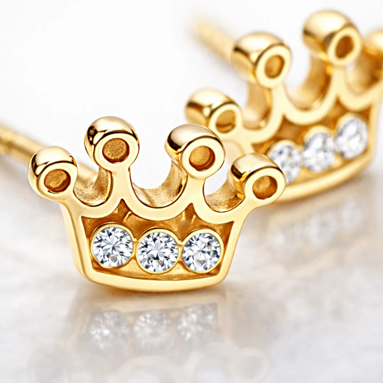 Zbliżenie złotych kolczyków w kształcie korony z białymi cyrkoniami
