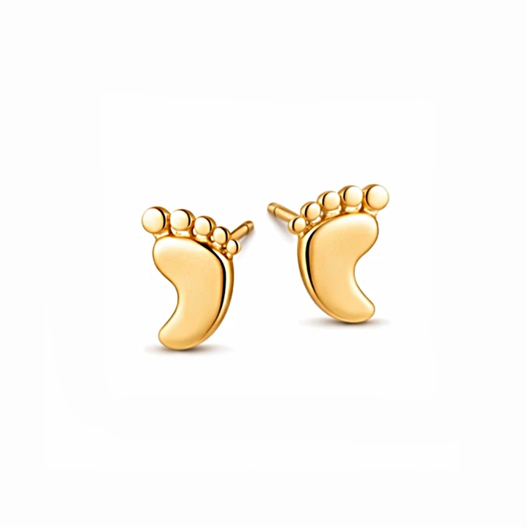 Złote kolczyki w kształcie stópek na białym tle